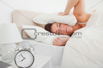 Pretty brunette woman awaking with a clock while lying