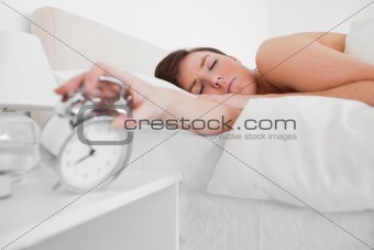 Beautiful brunette female awaking with a clock while lying
