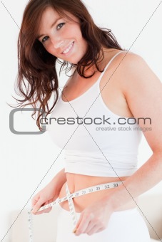 Attractive brunette woman measuring her belly with a tape measur