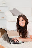 Charming brunette woman relaxing with her laptop while lying on 