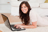 Pretty brunette woman relaxing with her laptop while lying on a 
