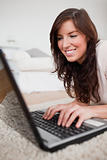Attractive brunette female relaxing with her laptop while lying 