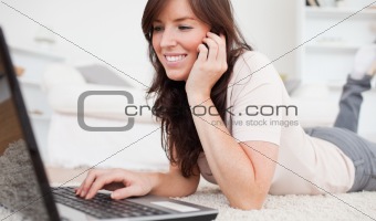 Pretty brunette woman on the phone while relaxing with her lapto