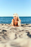 blonde girl in a black bathing suit lying on the shore of the blue sea