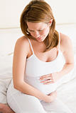 Pregnant woman sitting in bed holding stomach in pain