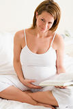Pregnant woman in bedroom reading book smiling