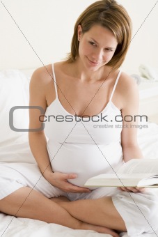 Pregnant woman in bedroom reading book smiling
