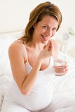 Pregnant woman in bedroom taking medicine holding water smiling