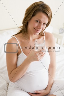 Pregnant woman sitting in bedroom with glass of water smiling