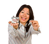 Attractive Multiethnic Woman Holding Small House and Keys Isolated on a White Background - Focus is on the house and keys.