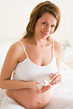 Pregnant woman in bedroom with medicine smiling