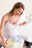 Pregnant woman packing baby clothing in suitcase holding list sm