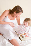 Pregnant woman in bedroom reading book with daughter laughing
