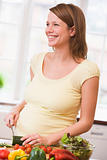 Pregnant woman in kitchen making a salad smiling