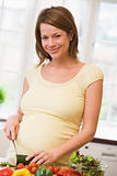 Pregnant woman in kitchen making a salad smiling