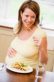 Pregnant woman in kitchen eating chicken and vegetables smiling