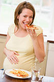 Pregnant woman in kitchen eating French fries and pizza smiling