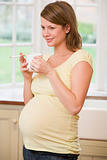Pregnant woman standing in kitchen with coffee and cigarette smi