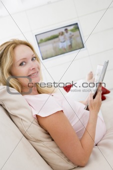 Pregnant woman reading magazine with television in background sm