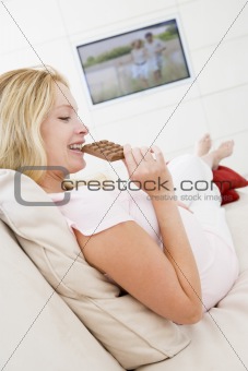 Pregnant woman watching television and eating chocolate smiling