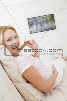 Pregnant woman watching television and eating chocolate smiling