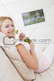 Pregnant woman watching television and eating pickles smiling