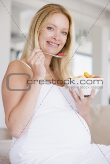 Pregnant woman with bowl of fruit salad smiling
