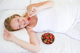 Pregnant woman lying in bed with bowl of strawberries smiling