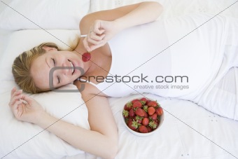Pregnant woman lying in bed with bowl of strawberries smiling