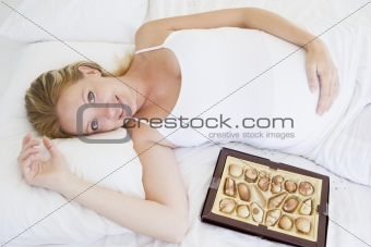 Pregnant woman lying in bed with chocolates smiling