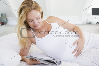 Pregnant woman lying in bed reading magazine smiling