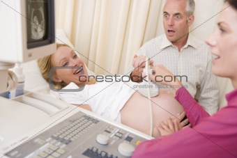 Pregnant woman getting ultrasound from doctor with husband watch