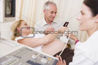Pregnant woman getting ultrasound from doctor with husband looki