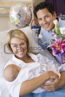 New mother with baby and husband in hospital smiling
