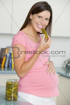 Pregnant woman in kitchen eating pickles and smiling