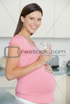 Pregnant woman in kitchen with glass of water smiling