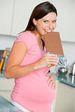 Pregnant woman in kitchen with large chocolate bar smiling