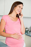 Pregnant woman in kitchen talking on cellular phone and smiling