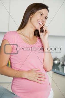 Pregnant woman in kitchen talking on cellular phone and smiling