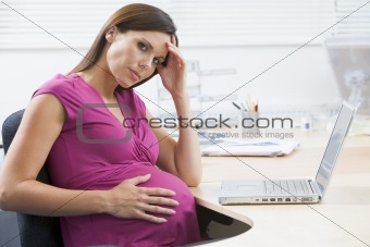 Pregnant woman at work with laptop looking stressed