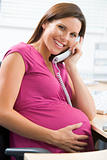 Pregnant woman at work using telephone smiling