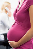 Pregnant woman at work holding belly with coworker in background