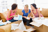 Three girl friends unpacking boxes in new home smiling