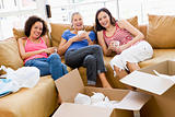 Three girl friends relaxing with coffee by boxes in new home smi