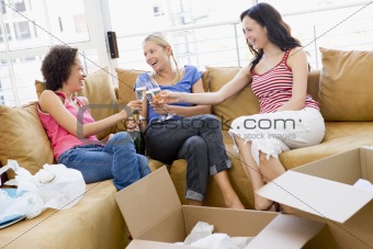 Three girl friends toasting champagne by boxes in new home smili