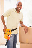 Man wearing tool belt standing by boxes in new home smiling