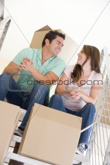 Couple sitting on staircase with boxes in new home smiling