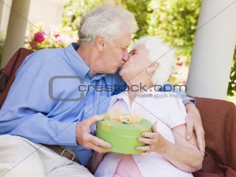 Husband giving wife gift on patio and kissing her