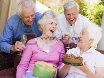 Two couples on patio with cake and gift smiling