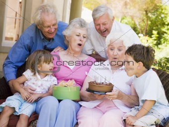 Grandparents and grandchildren on patio with cake and gift smili